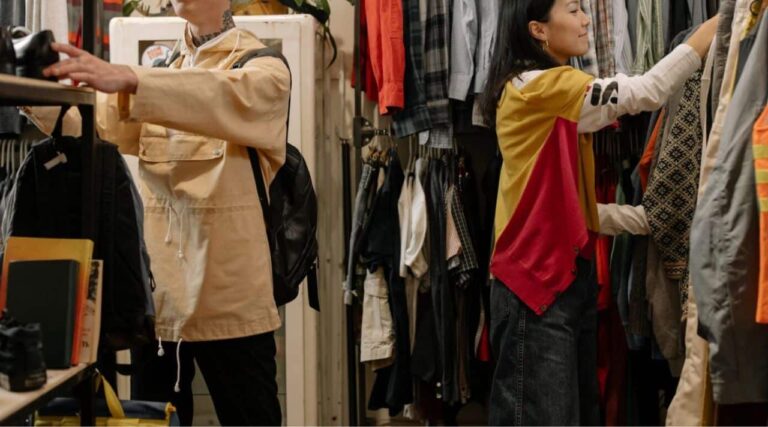 Shoppers learning how to thrift a gift while browsing secondhand clothing and household items in a thrift store